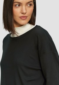 Zwarte sweatshirt met een ontspannen pasvorm, ronde halslijn en lange mouwen. Zachte textuur en gladde stof met een subtiele drape.