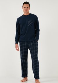 Mornarska majica s dugim rukavima za pidžamu s kariranim džepom, uparena s mornarskim hlačama s kockastim uzorkom koje imaju opušteni kroj. Mekani pamučni materijal.
