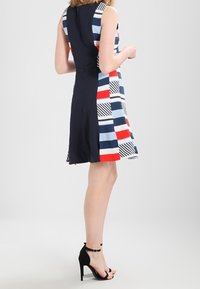 Vestido sin mangas con una mezcla de patrones geométricos en rojo, azul y blanco, y un lado negro. Tejido suave, de largo hasta la rodilla, con una silueta ajustada.