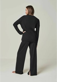 Schwarzer, gerippter Strickpullover mit langen Ärmeln, kombiniert mit weiten schwarzen Hosen. Beide Kleidungsstücke bieten eine lockere Passform und seitliche Schlitze.