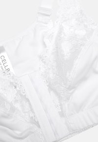 Soutien-gorge en dentelle blanche et tissu doux avec bretelles ajustables et fermeture à crochet ; présente de délicates bordures en dentelle sur les bonnets et des côtés lisses et sans coutures.