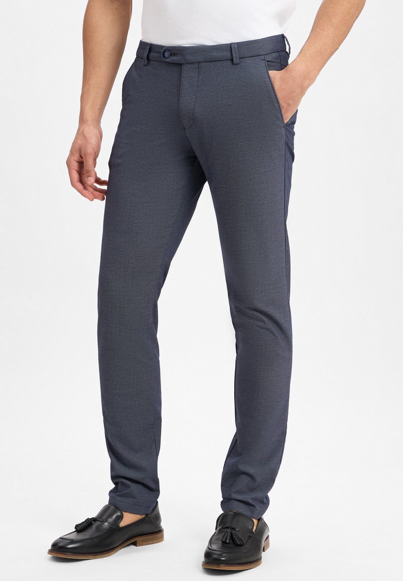 Navyblaue, maßgeschneiderte Hosen mit strukturierter Oberfläche, Gürtelschlaufen, Seitentaschen und slim fit, kombiniert mit schwarzen Quasten-Loafern.