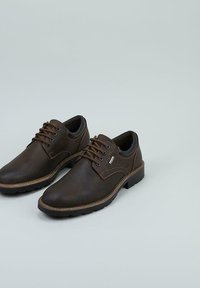 Par de zapatos de cuero marrón con cordones y suelas oscuras, costuras en contraste, y cuellos acolchados sobre un fondo gris claro.