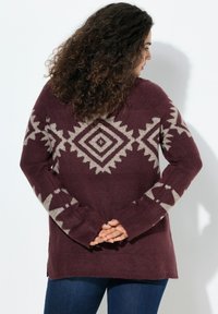 Burgunderfarbener Strickpullover mit geometrischen beigen Mustern, langen Ärmeln und seitlichen Schlitzen, im entspannten Schnitt und mit weichem Material.