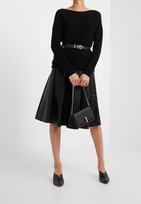 Pull noir côtelé avec un large col et des manches longues, associé à une jupe évasée en cuir noir. Accessoirisé avec un petit sac à main.