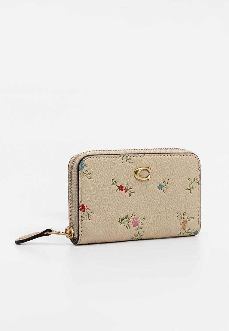 Beige Leder Geldbörse mit floralem Stickerei in Rot, Blau und Grün. Mit einem goldenen Logo und einem Reißverschluss mit einem Handgelenkriemen.