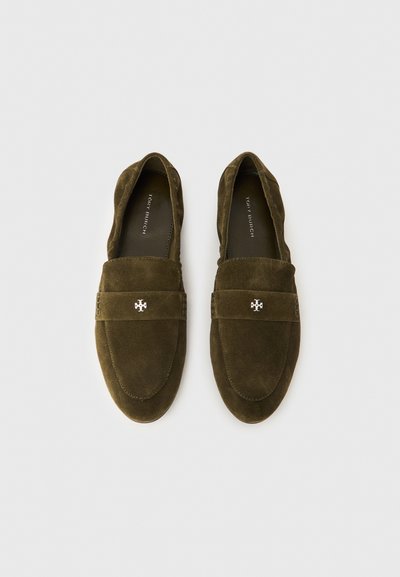 Olivzaļas krāsas zamšādas mokasīni ar plakanām zolēm, apaļu purngalu un dekoratīvu siksniņu ar emblēmu. Gluda tekstūra un vienkāršs dizains.