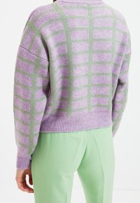 Dzianinowy sweter w kolorze lawendowym z zielonym wzorem w kratę, z szerokimi rękawami i prążkowanym obszyciem. Połączony z miętowozielonymi spodniami o prostych nogawkach.