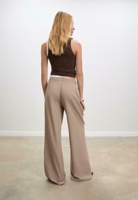 Bruine mouwloze top gecombineerd met losse beige wijde broek, met een elastische tailleband en een gladde stoftextuur.