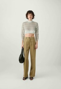 Crochet knit top with a scalloped pattern in light green, paired with high-waisted beige trousers and black sandals. Model holds a black bag.