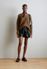 Brun strikket sweater, sorte lædershorts og sorte platform sandaler. Tørklæde bundet om halsen. Enkel design med en afslappet pasform.