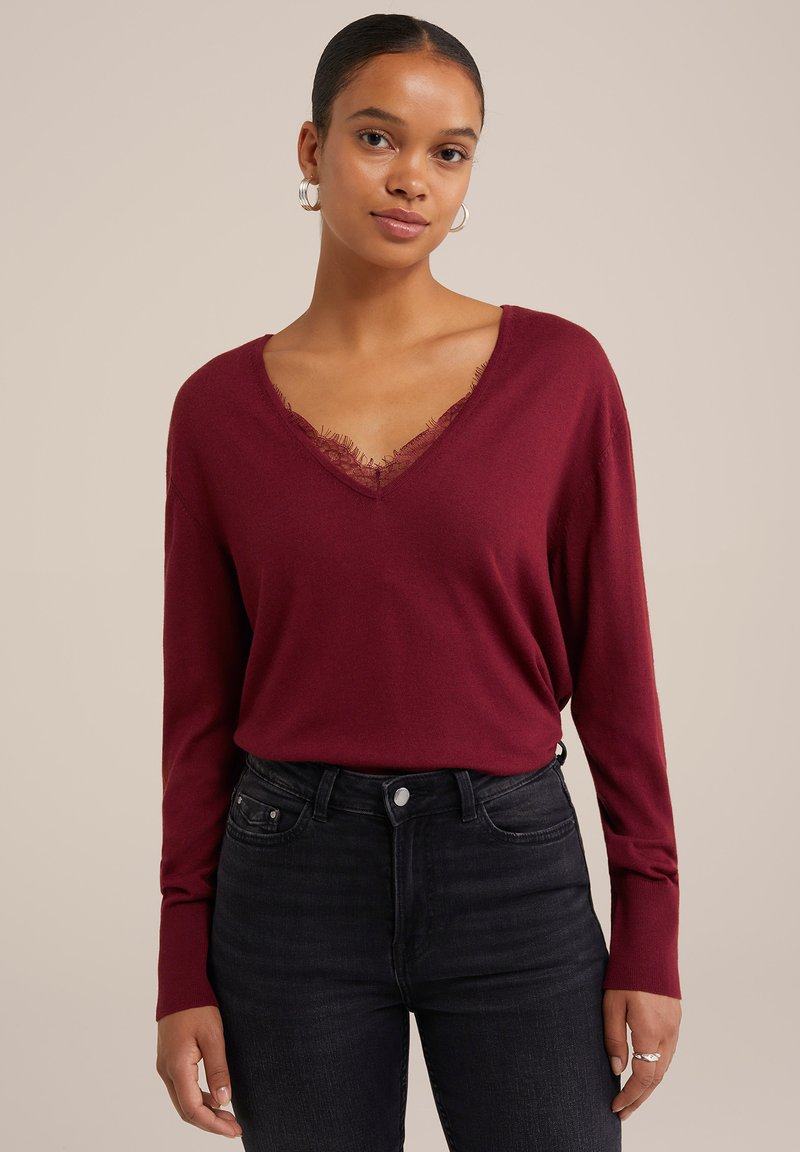 Top bordeaux a maniche lunghe con scollatura a V e bordo in pizzo, abbinato a jeans neri a vita alta. Include orecchini a cerchio argentati.