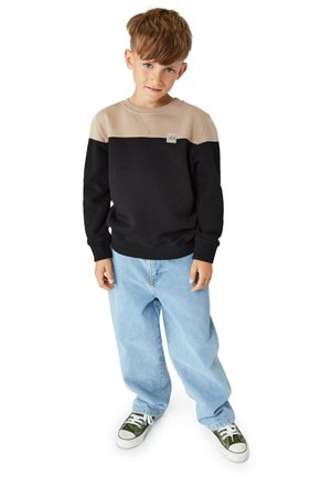 Schwarz-beige farblich abgesetzter Sweatshirt mit Logo-Patch, kombiniert mit hellblauen, locker geschnittenen Jeans und grün-weißen Sneakers.