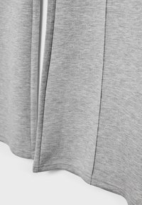 Gros plan sur un tissu gris avec des coutures verticales visibles et des ourlets cousus sur une surface textile douce et lisse.