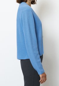 Ljust blå stickad cardigan med avslappnad passform, ruggad textur och långa ärmar, med rak fåll och minimal detaljering.