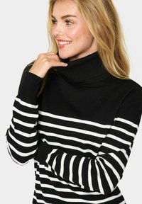 Black and white striped turtleneck sweater with ribbed texture and long sleeves, featuring contrasting horizontal stripes.