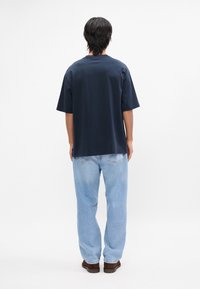 Μπλέ ναυτικό βαμβακερό μπλουζάκι με κοντά μανίκια, ελεύθερη γραμμή, στρογγυλή λαιμόκοψη και μονόχρωμο σχέδιο. Συνδυασμένο με ανοιχτό μπλε τζιν παντελόνι και καφέ παπούτσια.