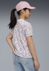 T-shirt med kort ärm i krämfärgad med ett sv�ängande mönster i lila och rosa, tillsammans med ljusblå jeans och en ljusrosa keps.