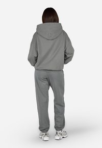 Szürke kapucnis pul�óver laza szabással, hozzá illő melegítőnadrággal párosítva. Puha tapintású anyag ribbelt mandzsettákkal és fehér sportcipőkkel.