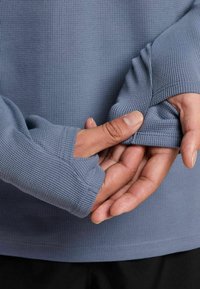 Blau geripptes Langarmshirt mit Daumenlöchern an den Manschetten. Weiche Textur und taillierte Passform, perfekt für Lagenlooks oder für aktive Kleidung.