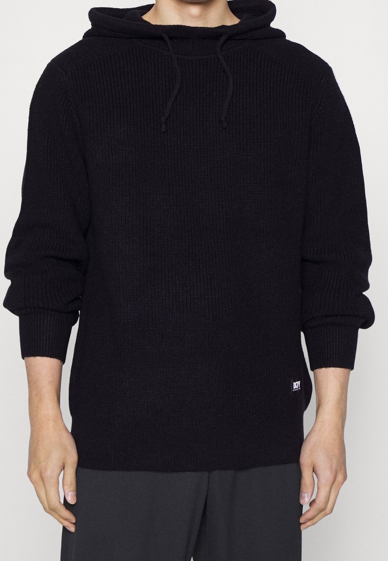 Hoodie noir en tricot avec un motif texturé, cordon de serrage et poignets côtelés. Dispose d'un patch logo à l'ourlet. Silhouette droite.