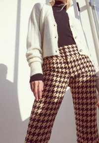 Krémový kardigan s ribbovanou texturou, zapínání na knoflíky přes černý rolák. Kalhoty mají velký houndstooth vzor v béžové a černé barvě.