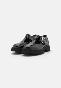 Sapatos de verniz pretos com solas grossas, tira T e detalhe em fivela prateada. Apresenta bico redondo e piso texturizado.
