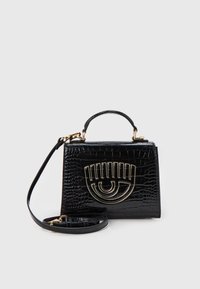 Svart krokodilprägling handväska med övre handtag, avtagbar axelrem och gyllene ögonformerad metalldetalj på framsidan.