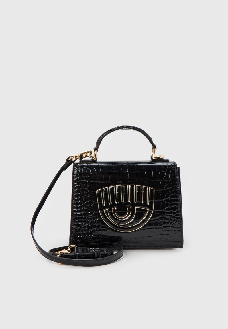 Svart krokodilprägling handväska med övre handtag, avtagbar axelrem och gyllene ögonformerad metalldetalj på framsidan.