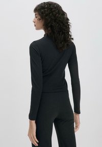 Schwarzes Langarmshirt aus weichem Stoff, mit einer figurbetonten Passform und hohem Kragen. Der Rücken ist glatt mit leichtem Stretch.