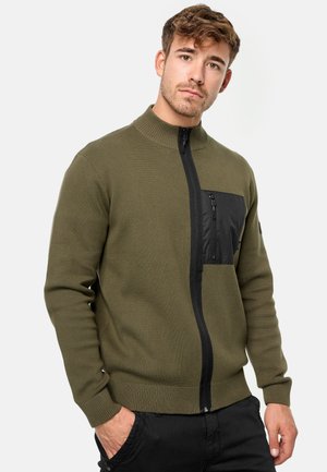 Olivgrüner Zip-Up-Pullover mit hohem Kragen, schwarzem Nylon-Brusttasche, gerippten Bündchen und Saum, der aus einem strukturierten Strickstoff gefertigt ist.