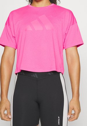 Kvinde iført en lyserød cropped sportsbluse med sorte og grå højtaljede træningsshorts.