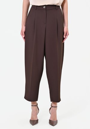Donna che indossa pantaloni corti a vita alta di colore marrone scuro abbinati a décolleté marroni a punta con cinturino alla caviglia.