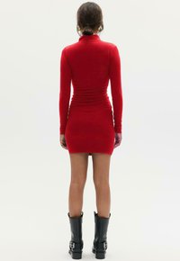 Rode mini-jurk met lange mouwen, aansluitend ontwerp en gerimpelde textuur. Gestyled met zwarte kniehoge laarzen met gespen.