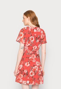 Vestido florido em coral, feito de um tecido leve. Mangas curtas, cintura ajustada, saia rodada, com grandes flores brancas e pink.