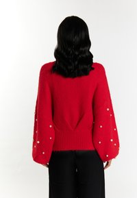 Pulover roșu din tricot, cu mâneci balon, având accente de perlă pe manșete și un tiv rib knit. Textură moale și croială lejeră.