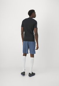 T-shirt de sport noir et blanc, shorts bleus, chaussettes blanches et crampons noirs. Dispose d'un design ajusté avec des manches courtes et des bandes latérales.