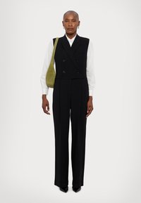Chaleco negro de doble botonadura con corte entallado, combinado con pantalones de tiro alto. Camisa blanca debajo y bolso de hombro de ante verde como acento.