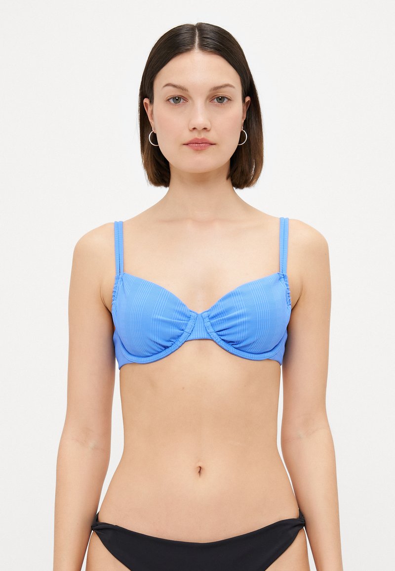 Top bikini blu ribbed con supporto in filigrana, dotato di spalline regolabili e design centrale attorcigliato. Abbinato a un bikini bottom nero.