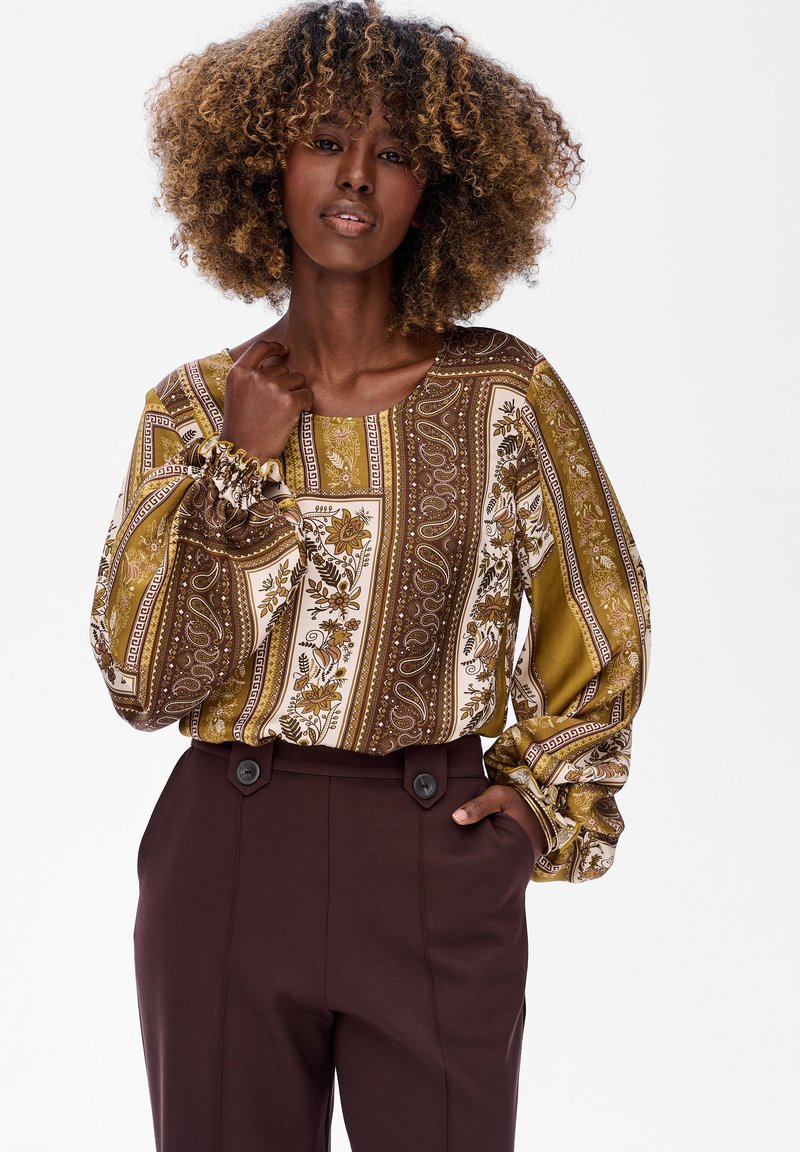 Bluzka z długim rękawem w wzór paisley i kwiatowy w brązowych i oliwkowych odcieniach; bufiaste rękawy z marszczonymi mankietami; w komplecie z brązowymi spodniami z wysokim stanem.