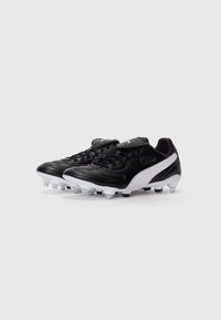Botas de fútbol en blanco y negro con cubiertas de cordones y tachuelas de plástico, posicionadas una al lado de la otra sobre un fondo blanco.