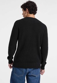 Schwarzer Rippstrickpullover mit langen Ärmeln und Rundhalsausschnitt. Verfügt über eine strukturierte Oberfläche und eine taillierte Passform. Kombiniert mit blauen Jeans.