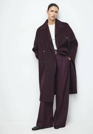 Burgundy double-breasted coat with wide lapels, paired with high-waisted, loose-fit trousers in a matching shade and black footwear.