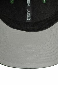 Casquette de baseball avec une visière noire et un tissu gris en dessous, comportant une texture subtile et des détails de couture. La bande intérieure présente le logo et la taille.