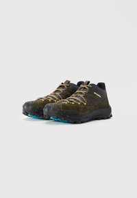 Chaussures de randonnée vert foncé et noires avec des lacets jaune et noir et des semelles robustes à bout bleu, inclinées vers la gauche sur un fond blanc uni.