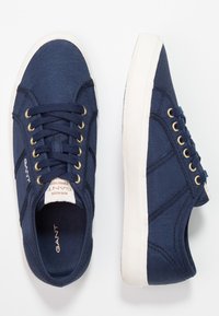 Baskets en toile bleu marine avec œillets en métal doré, semelle en caoutchouc blanche et détails de logo. Caractérisées par un matériau texturé et une semelle intérieure rembourrée.