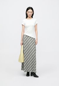 En hvid t-shirt med korte ærmer kombineret med en lang gråstribet nederdel. Modellen holder en gul taske og har sorte støvler med hæl på.