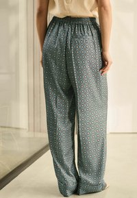 Patroon losse broek in teal, met een subtiel bloemenontwerp, een elastische tailleband en een zak aan de achterkant.