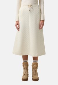 Cremfarbene, gesteppte Midirock mit Kordelzugbund, kombiniert mit beige, fellgefütterten Stiefeln und weißen Socken. Die Textur zeichnet sich durch ein geometrisches Muster aus.