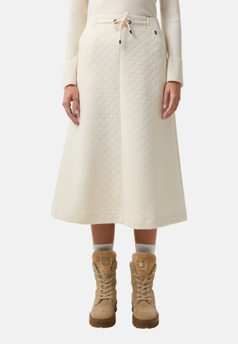 Cremfarbene, gesteppte Midirock mit Kordelzugbund, kombiniert mit beige, fellgefütterten Stiefeln und weißen Socken. Die Textur zeichnet sich durch ein geometrisches Muster aus.